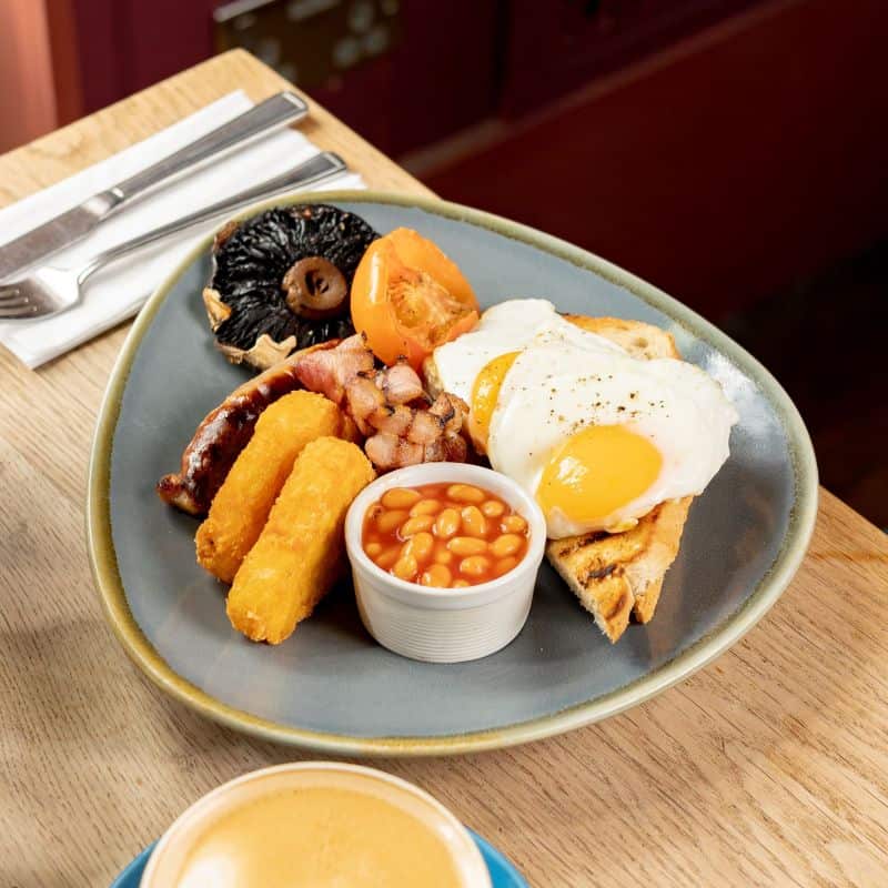 Full English Breakfast on a grey plate. A coffee is sat next to the breakfast plate