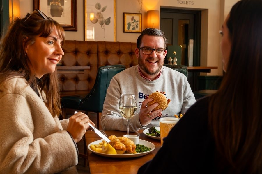 3 people around a pub table eating food and drink